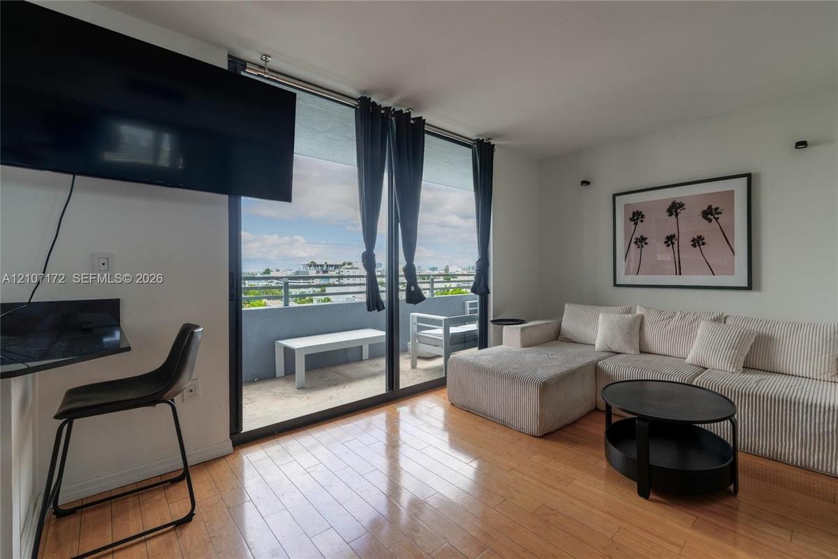 Floor-to-ceiling sliding glass doors, private balcony, wood-finish flooring, and wall-mounted lighting