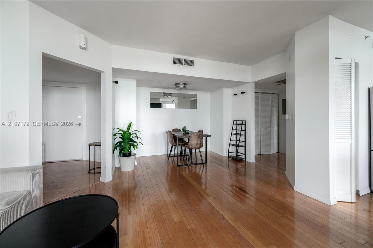 Open-concept interior featuring wood-finish flooring, a flush-mount ceiling light fixture, a wall-mounted rectangular mirror, and double-door closet c