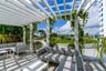 Outdoor terrace featuring a white overhead trellis, built-in stainless steel kitchen station, stone-surfaced flooring, and perimeter planters