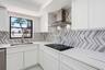 White shaker-style cabinetry with minimalist hardware, white countertops, and a full-height chevron-patterned tile backsplash