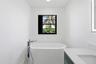 Freestanding soaking tub with floor-mounted chrome faucet, black-framed window, vanity with integrated sink, and illuminated mirror