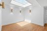Skylight with natural light, wood-finish flooring, white walls, and three gold-tone wall sconces