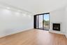Spacious room with wood-finish flooring, a white marble fireplace, recessed ceiling lighting, and black framed glass sliding doors leading to a balcon