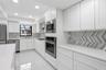 White cabinetry, stainless steel appliances, herringbone-patterned backsplash, recessed lighting, and a window above the sink
