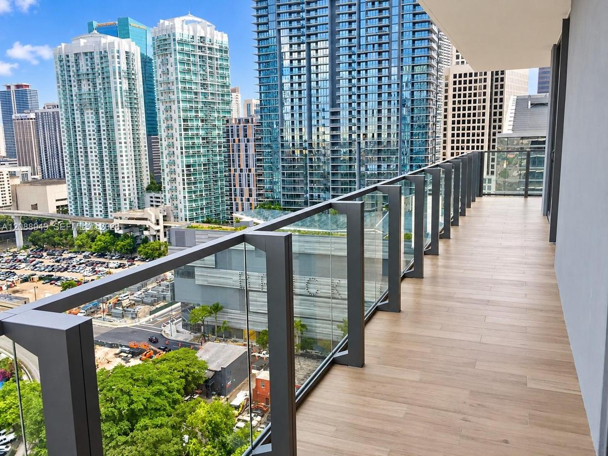 Expansive private balcony featuring wood-finish tile flooring and a sleek frameless glass railing system with dark metal supports