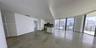 Open-concept interior featuring large-format tile flooring, floor-to-ceiling windows, and a kitchen equipped with a central island and stone-surfaced 