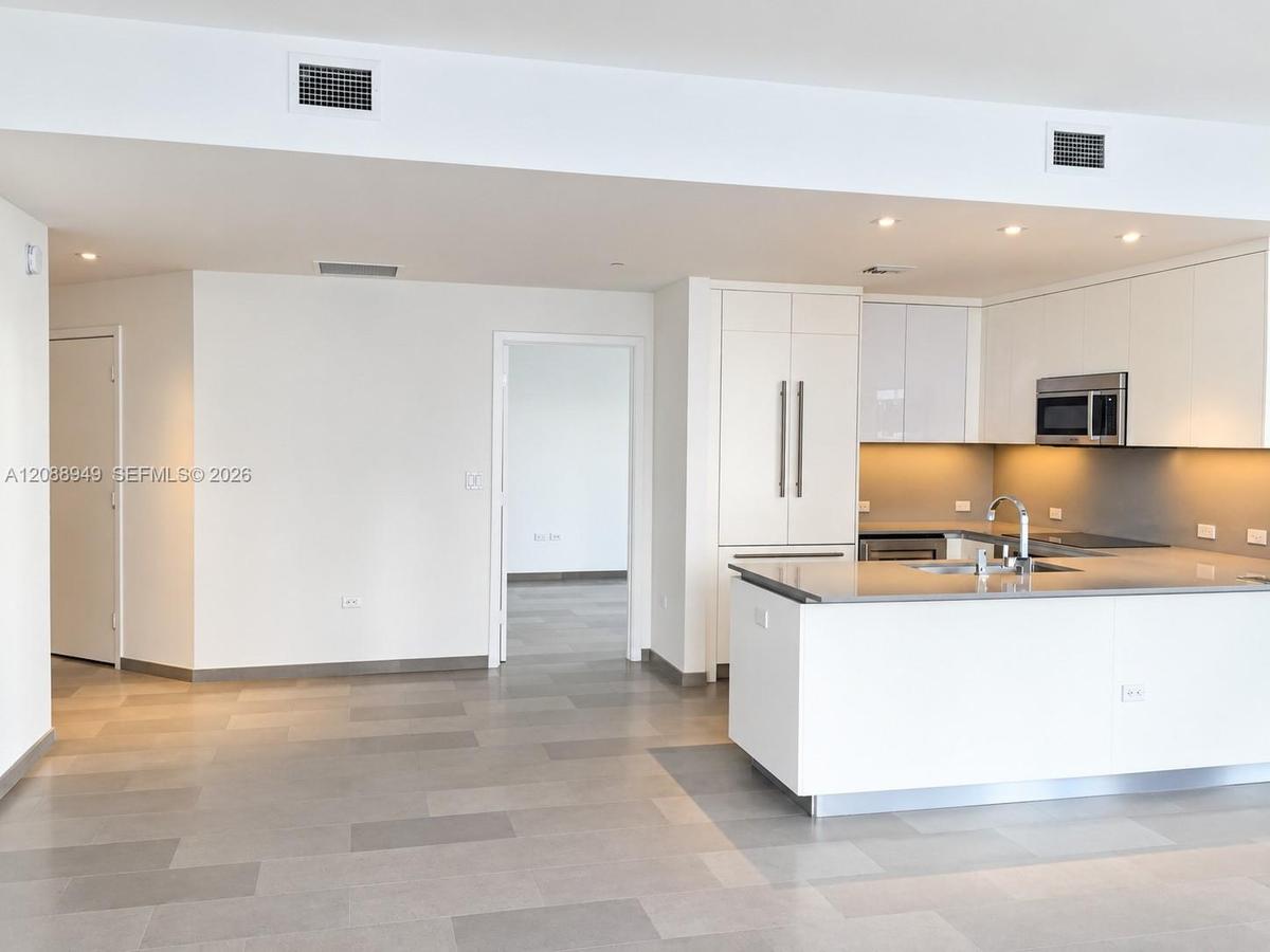 Modern kitchen featuring white flat-panel cabinetry, a central island with a solid-surface countertop, stainless steel appliances, and neutral-tone ti