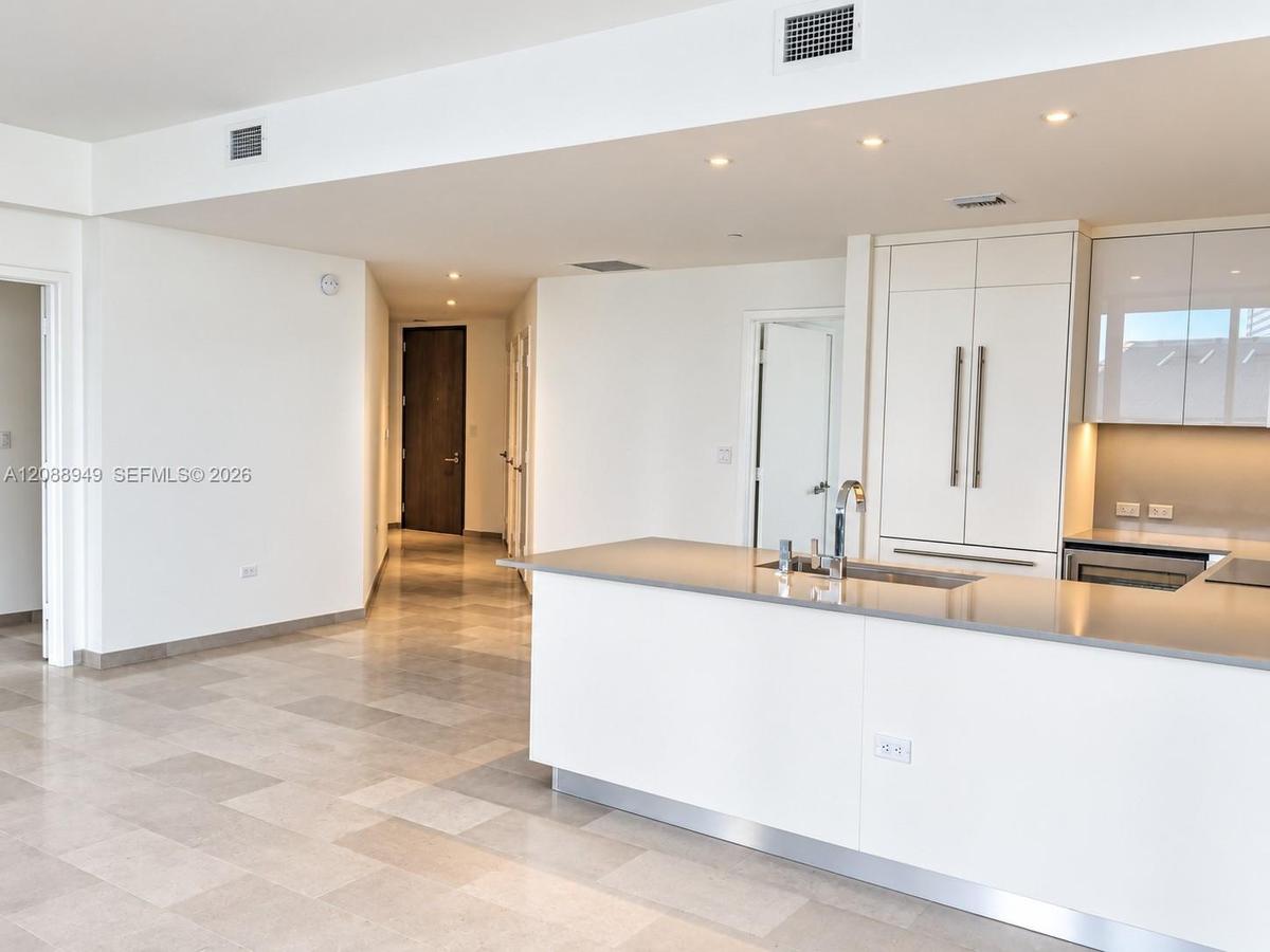 Modern kitchen featuring white flat-panel cabinetry, stone-finish countertops, recessed lighting, and large-format tile flooring