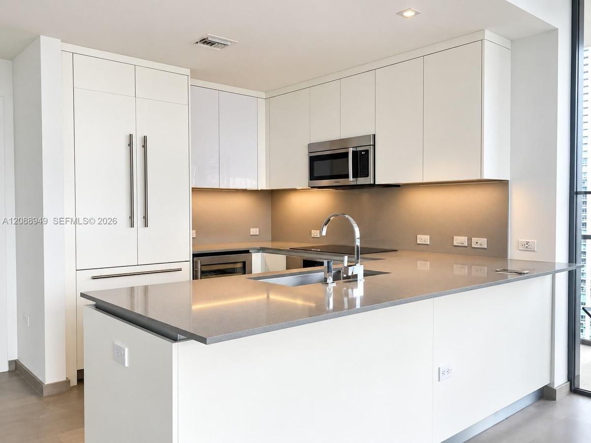 Modern kitchen featuring flat-panel white cabinetry, solid-surface countertops, an undermount sink with a gooseneck faucet, stainless steel microwave,