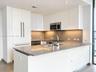 Modern kitchen featuring flat-panel white cabinetry, solid-surface countertops, an undermount sink with a gooseneck faucet, stainless steel microwave,