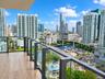 Private balcony featuring wood-finish flooring and glass panel railings with dark metal framing, overlooking an urban cityscape and waterway