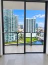 Full-height sliding glass doors with dark metal frames, wood-finish flooring, and a private balcony featuring a glass panel railing