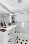 White shaker-style vanity with a solid surface countertop, undermount sink, integrated LED-backlit mirror, bathtub with glass sliding doors, and hexag