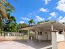 Covered concrete carport with integrated support pillars, gated perimeter fencing, and concrete driveway surface