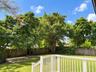 Backyard featuring a wood deck with white railings, a concrete patio, perimeter wood fencing, and mature trees