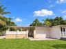Rear exterior featuring a covered patio, stucco and masonry wall, integrated carport, concrete flooring, and manicured lawn