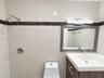 Bathroom featuring floor-to-ceiling cream tiling with dark stone accent banding, a vanity with an integrated basin, wall-mounted brushed-metal hardwar