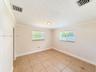Neutral-toned interior featuring large-format square tile flooring, crown molding, dual windows with horizontal blinds, and a centered flush-mount cei