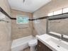 Full-height neutral stone tiling with decorative dark stone accent banding, modern wood-finish vanity with integrated rectangular sink, wall-mounted m
