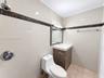 Bathroom featuring light-toned wall tile with dark stone accent trim, wood-finish vanity with a rectangular sink, wall-mounted light fixture, and meta
