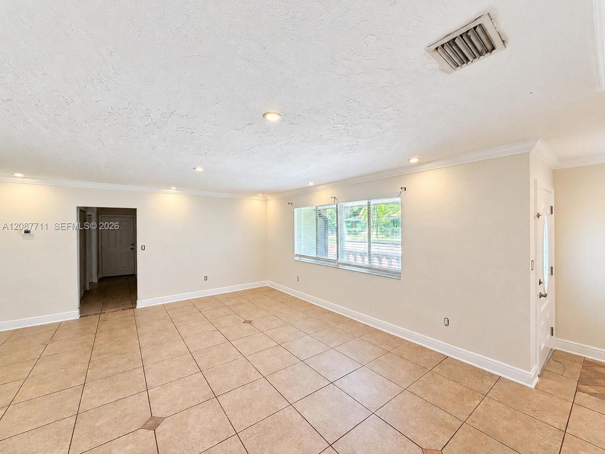 Neutral-toned tile flooring with decorative inserts, recessed lighting, crown molding, and large windows