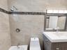 Bathroom featuring floor-to-ceiling tile with a contrasting decorative inlay, a wood-finish vanity with a white countertop and integrated sink, a cont