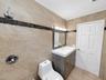 Full-wall tile surround with dark stone accent banding, wood-finish vanity with integrated sink, four-light vanity fixture, and six-panel interior doo