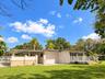 Single-story residence featuring an attached carport, covered side porch with decorative pillars, white railing, and a spacious lawn