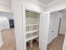 Built-in storage closet featuring custom shelving, louvered white door, decorative door casing, and tile flooring