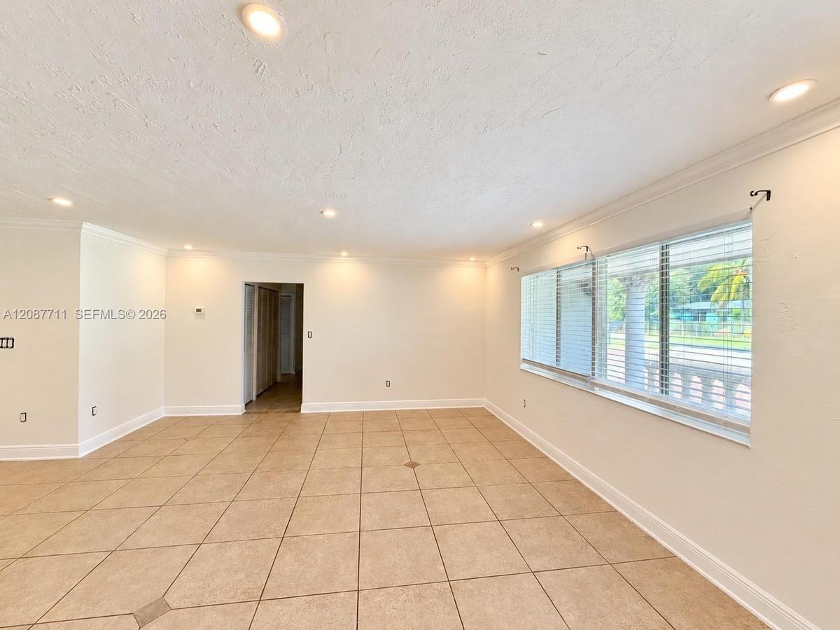 Neutral-toned tile flooring, recessed lighting, expansive multi-pane window with horizontal blinds, and crown molding