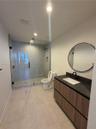 Floating vanity featuring wood-finish cabinetry, dark countertop, and integrated rectangular sink, paired with a frameless glass-enclosed shower, matt