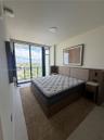 Floor-to-ceiling glass sliding doors opening to a balcony, tile flooring, and a built-in wood-finish headboard with integrated side tables