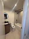 Bathroom featuring a wood-finish vanity with a dark stone countertop, circular mirror, and matte black hardware including a shower-tub faucet assembly