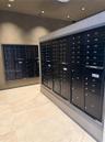 Integrated mail station featuring matte black secure postal lockers, neutral stone-finish tile flooring, recessed ceiling lighting, and smooth, monoch