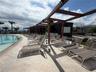 Curved swimming pool with stone-tiled decking and an overhead wooden pergola structure