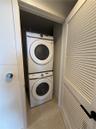 Stacked laundry center featuring high-efficiency washer and dryer, tile flooring, and louvered closet door