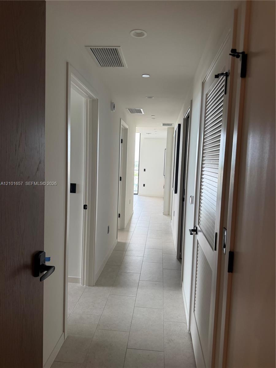 Hallway featuring large-format ceramic tile flooring, recessed ceiling lighting, and matte black hardware on solid-core wood doors, including a louver
