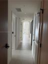 Hallway featuring large-format ceramic tile flooring, recessed ceiling lighting, and matte black hardware on solid-core wood doors, including a louver