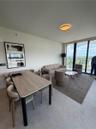 Open-concept interior featuring floor-to-ceiling glass windows, neutral tile flooring, modern circular ceiling lighting, and a glass-railed balcony