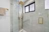 Walk-in shower featuring floor-to-ceiling stone-finish tile, glass enclosure, gold-tone hardware, rainfall showerhead, and a rectangular niche