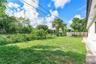 Spacious backyard featuring a grass lawn, mature palm trees, perimeter wood fencing, and a detached storage shed