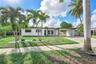 Single-story exterior featuring white stucco siding, a covered carport, decorative breezeblock wall accents, and mature palm trees