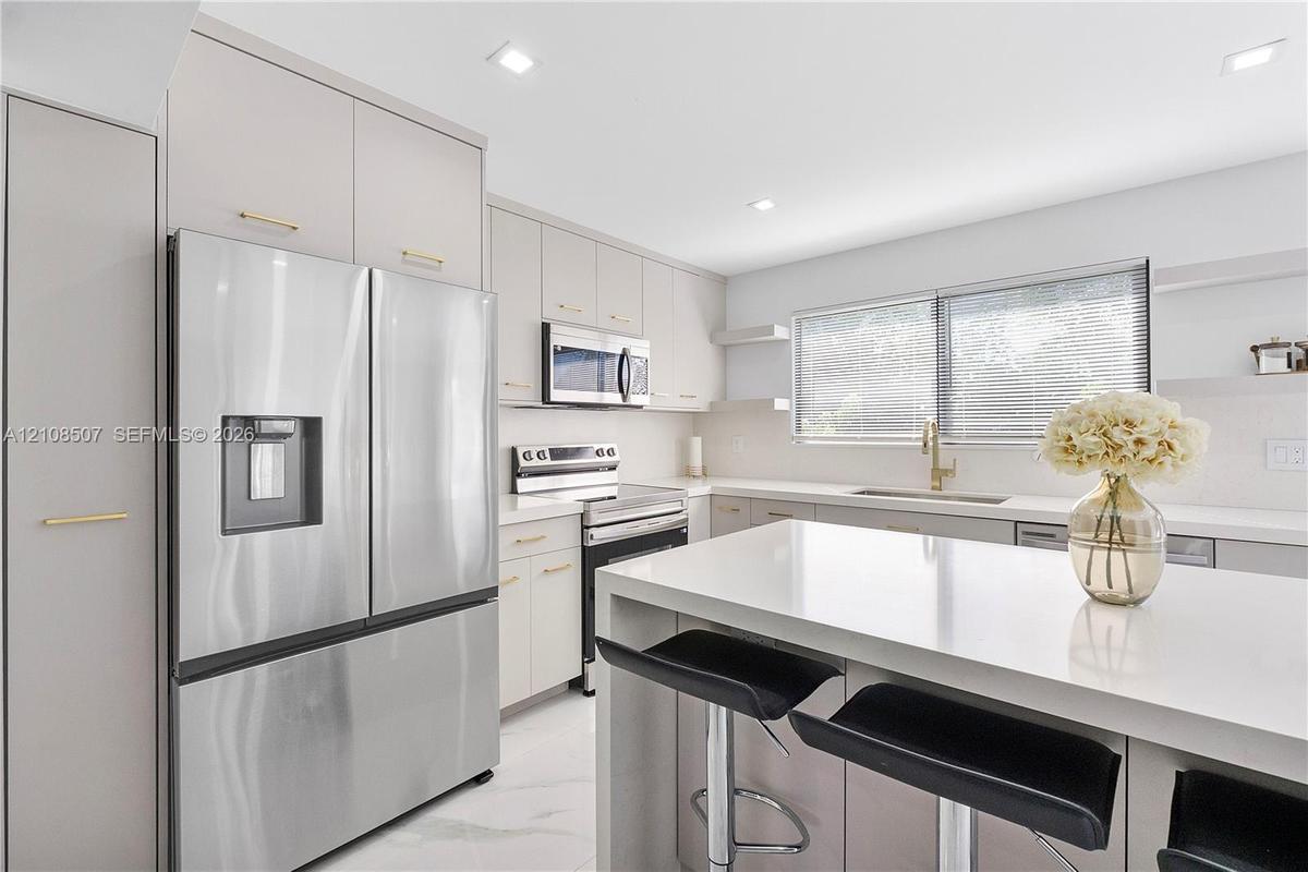 Kitchen featuring flat-panel cabinetry with gold-tone hardware, a central island with a solid-surface countertop, stainless steel appliances, and rece