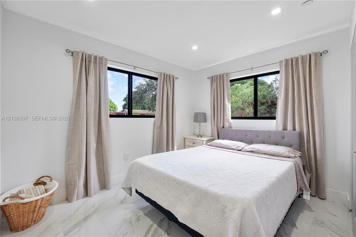 Neutral-toned room featuring large windows with black frames, recessed lighting, and white stone-finish tile flooring