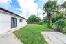 Exterior side yard featuring white stucco siding, double-pane glass French doors, a concrete patio, and mature palm landscaping