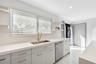Kitchen featuring light-toned cabinetry, solid surface countertops, a stainless steel undermount sink with a brass-finish faucet, built-in stainless s