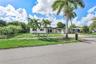 Single-story residence featuring a white stucco exterior, attached carport with decorative breeze block screen, concrete driveway, and mature palm tre