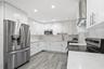 Kitchen featuring white shaker-style cabinetry, stainless steel appliances, stone-finish countertops, full-height backsplash, and wood-finish flooring