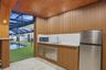 Covered outdoor kitchen featuring vertical wood-paneled walls and ceiling, stainless steel refrigerator, undermount sink with gooseneck faucet, and bu