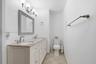 Double vanity featuring a stone countertop, dual undermount sinks, shiplap-style cabinetry, a framed mirror, and brushed-nickel lighting and fixtures